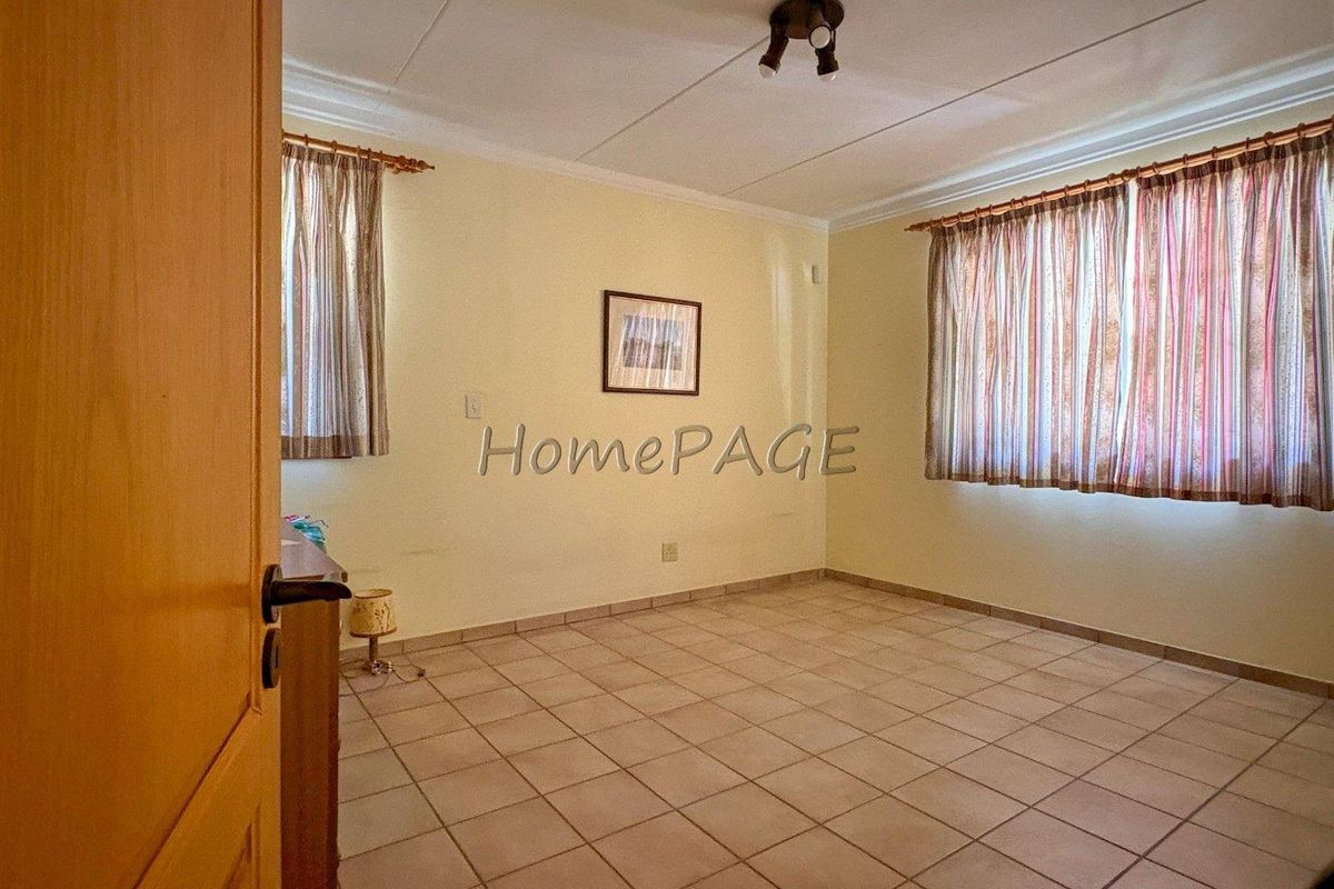 A spacious bedroom featuring tiled flooring, neutral walls, and large windows with curtains, offering a clean and functional living space.