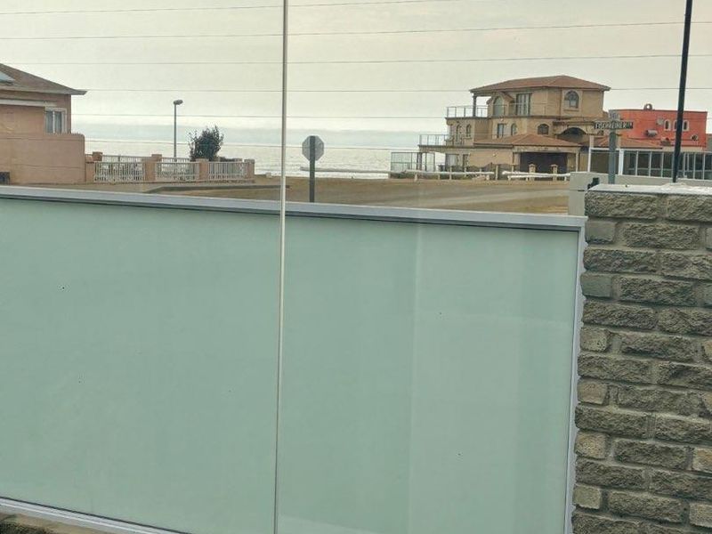A view of the coastal neighbourhood and ocean horizon, framed by a modern glass balustrade and stone-clad wall.