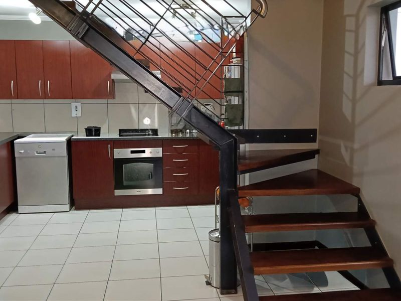 A functional kitchen featuring dark wood cabinetry, built-in oven and hob, tiled flooring, and an integrated metal staircase leading to the upper level.