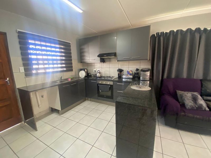 Open-plan kitchen featuring modern dark cabinetry, granite countertops, built-in oven and hob, and tiled flooring, seamlessly flowing into the adjacent living area.