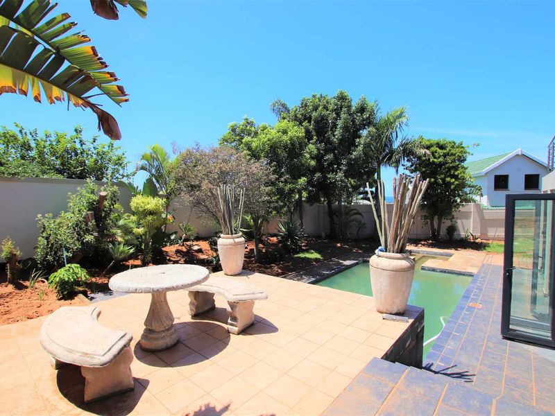 Outdoor entertainment area featuring a tiled patio, swimming pool, and established garden with boundary walling.