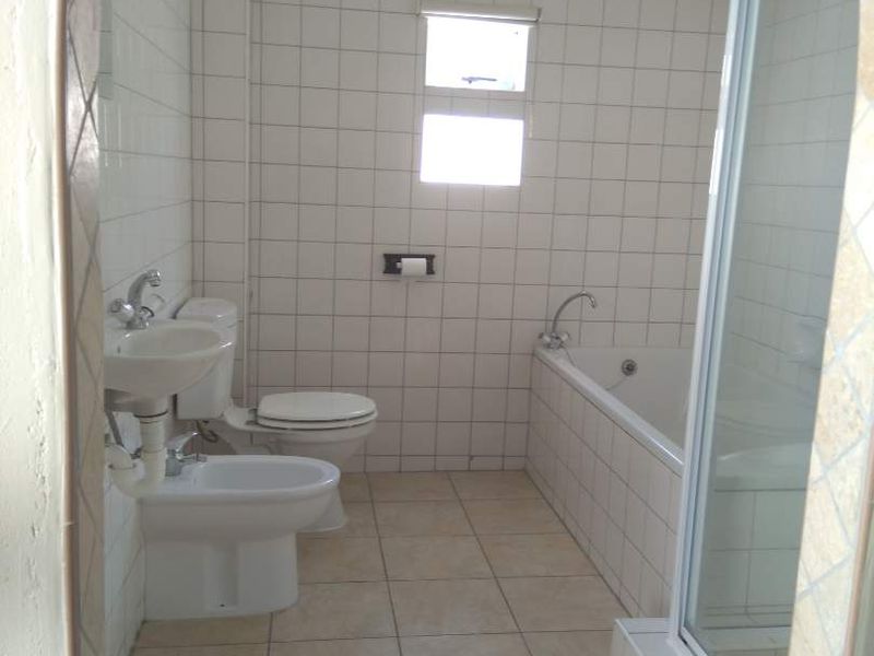 A functional bathroom featuring a bathtub, separate shower enclosure, toilet, bidet, and pedestal basin with full-height wall tiling.