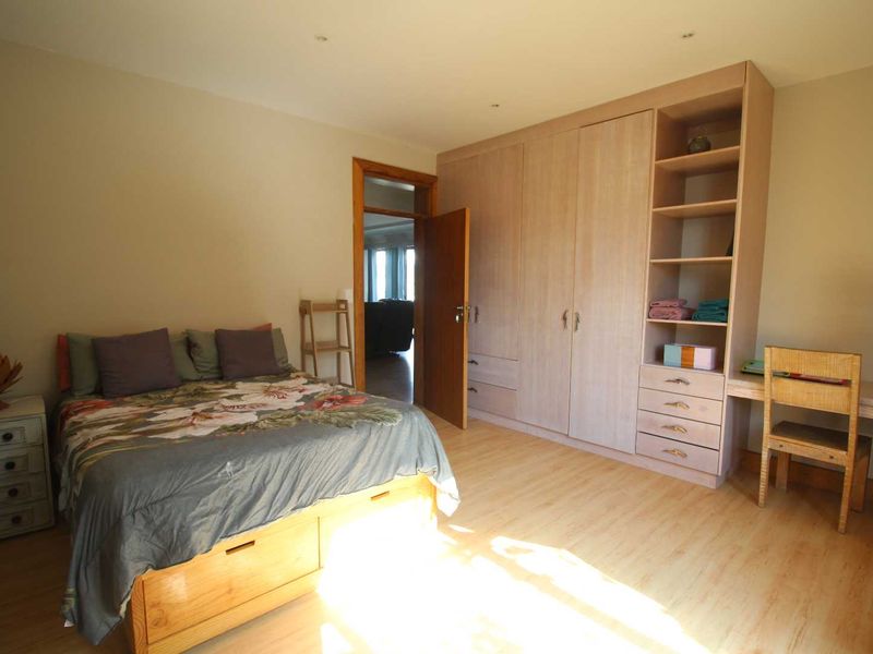 A well-lit bedroom featuring light wood-tone laminate flooring, extensive built-in cabinetry including a wardrobe, shelving, and a desk area.