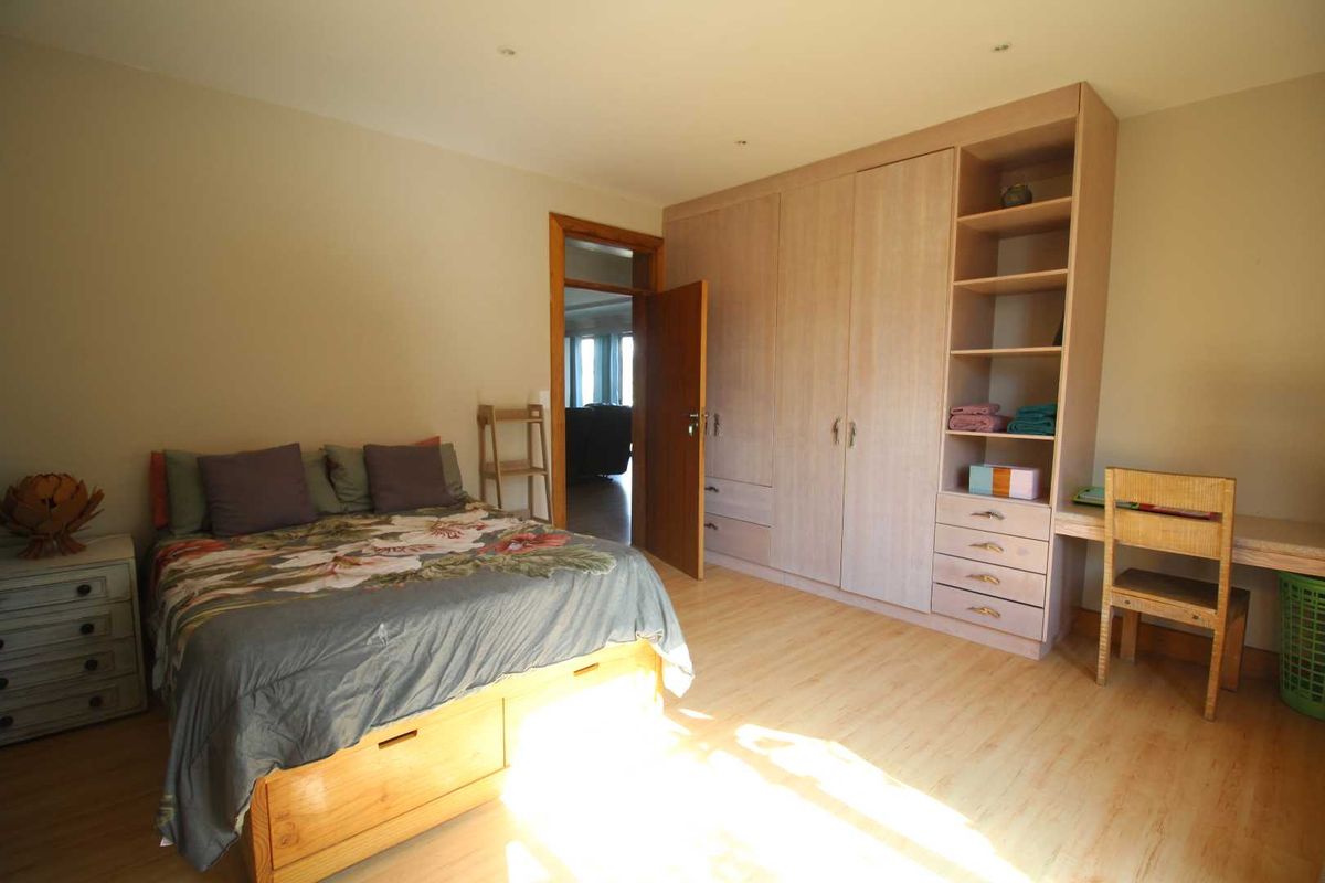 A well-lit bedroom featuring light wood-tone laminate flooring, extensive built-in cabinetry including a wardrobe, shelving, and a desk area.