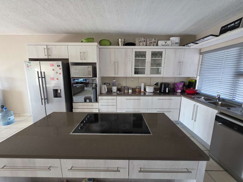 A functional kitchen featuring light wood-look cabinetry, a central island with an integrated electric hob, and ample counter space with a double sink.