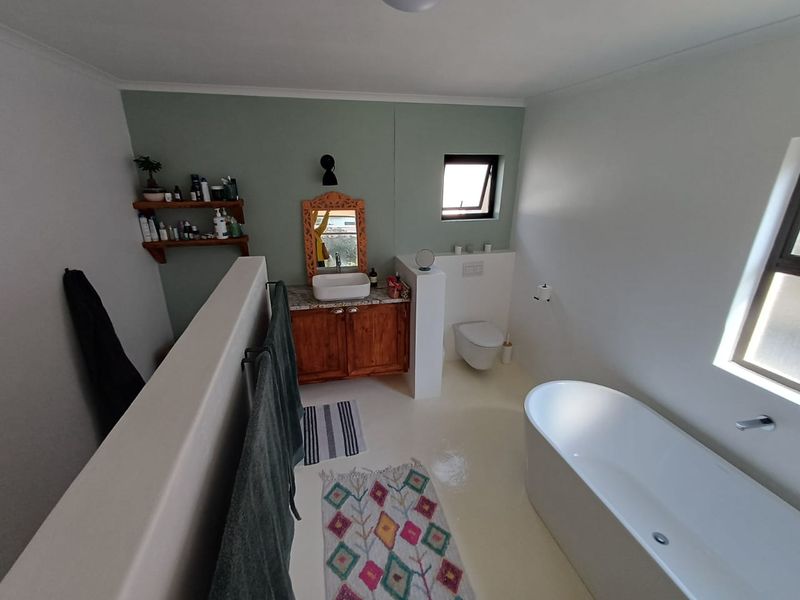 Modern bathroom featuring a freestanding bathtub, wall-hung toilet, and a wooden vanity with a vessel sink, finished with a soft green accent wall.
