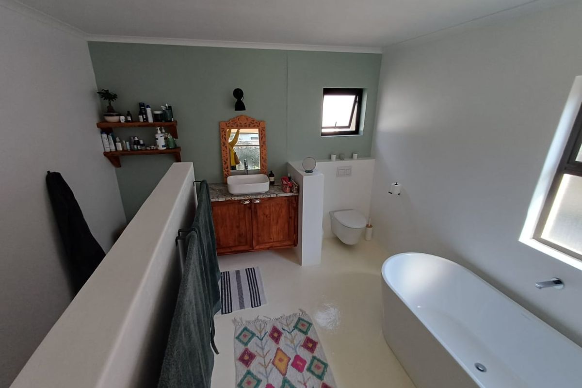 Modern bathroom featuring a freestanding bathtub, wall-hung toilet, and a wooden vanity with a vessel sink, finished with a soft green accent wall.