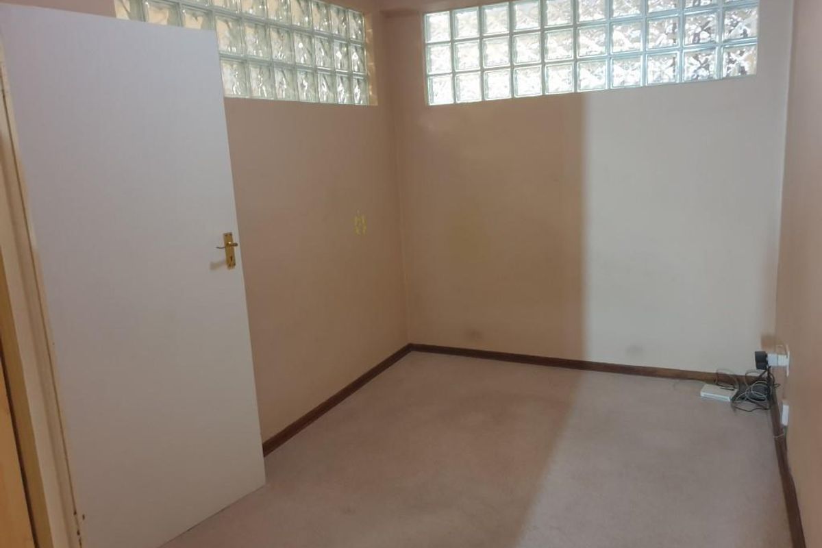An empty bedroom featuring neutral walls, carpeted flooring, and high-level glass block windows providing natural light.