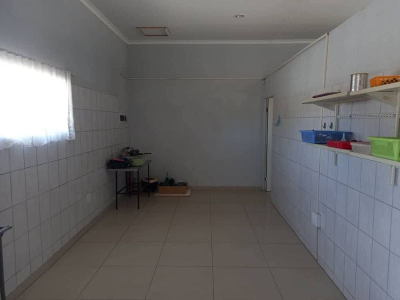 A functional, empty scullery or utility space featuring tiled walls, tiled flooring, and wall-mounted shelving units.