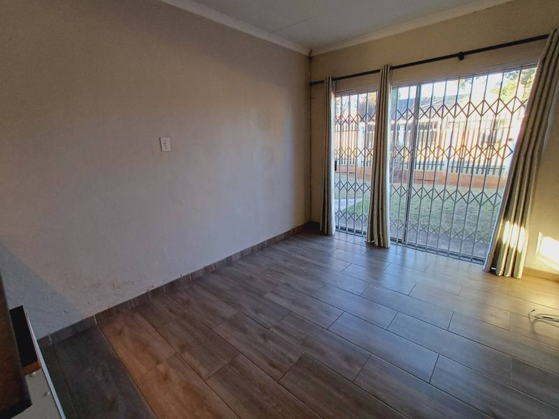An empty living room featuring wood-look tile flooring, a sliding glass door with security gate, and neutral wall finishes.