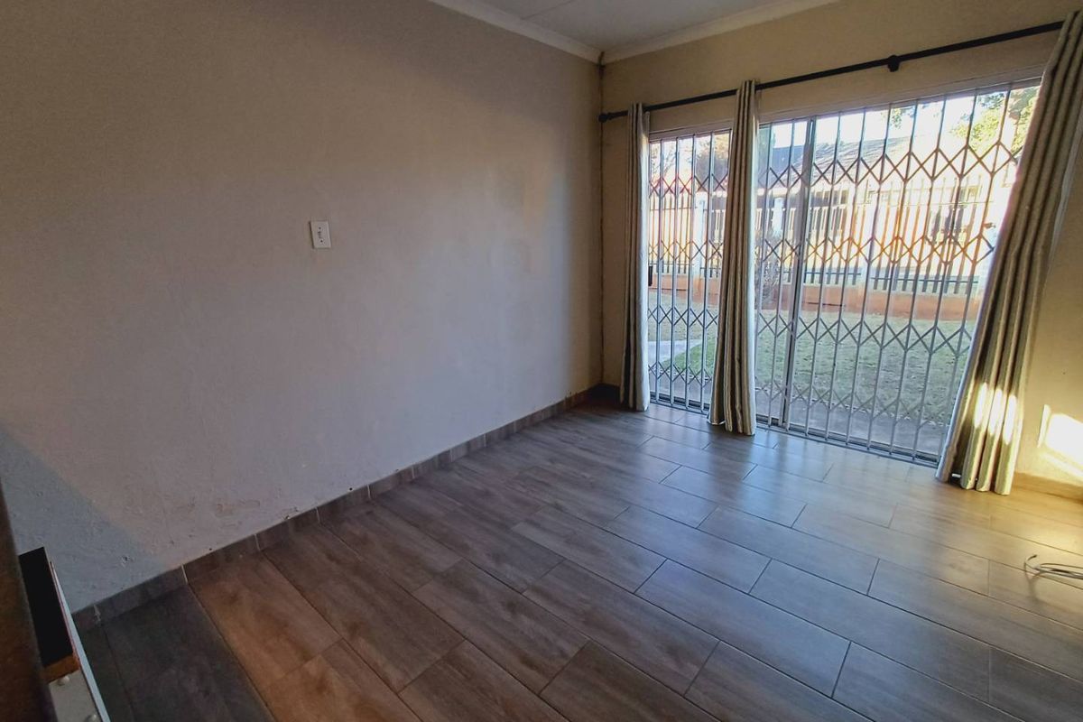 An empty living room featuring wood-look tile flooring, a sliding glass door with security gate, and neutral wall finishes.