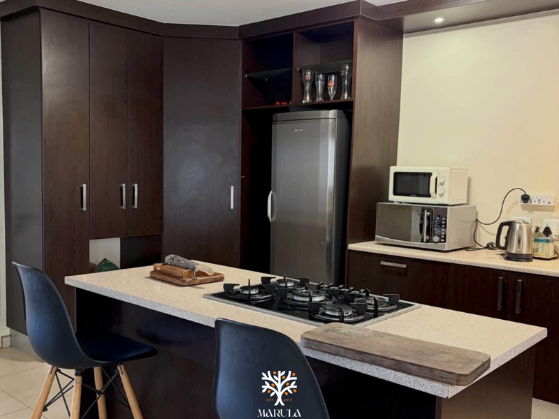 Modern kitchen featuring dark wood cabinetry, stone countertops, and a central island with a built-in gas hob.