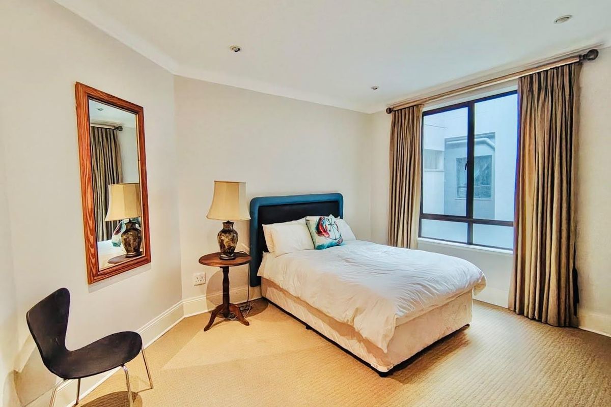 A well-maintained bedroom featuring neutral carpeting, recessed downlighting, and a large window with curtain tracks, providing a bright and comfortable living space.