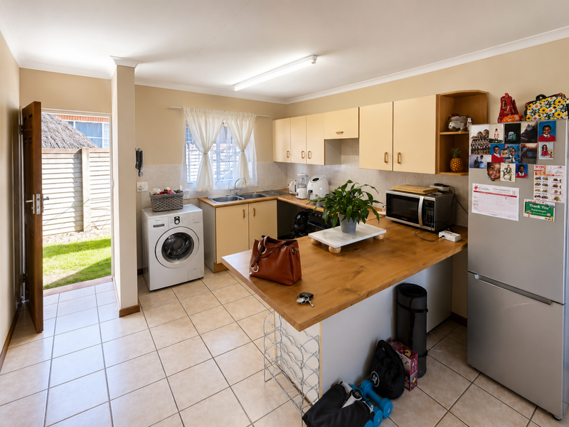 A functional kitchen featuring built-in cabinetry, a wooden breakfast bar, tiled flooring, and direct access to the rear garden area.