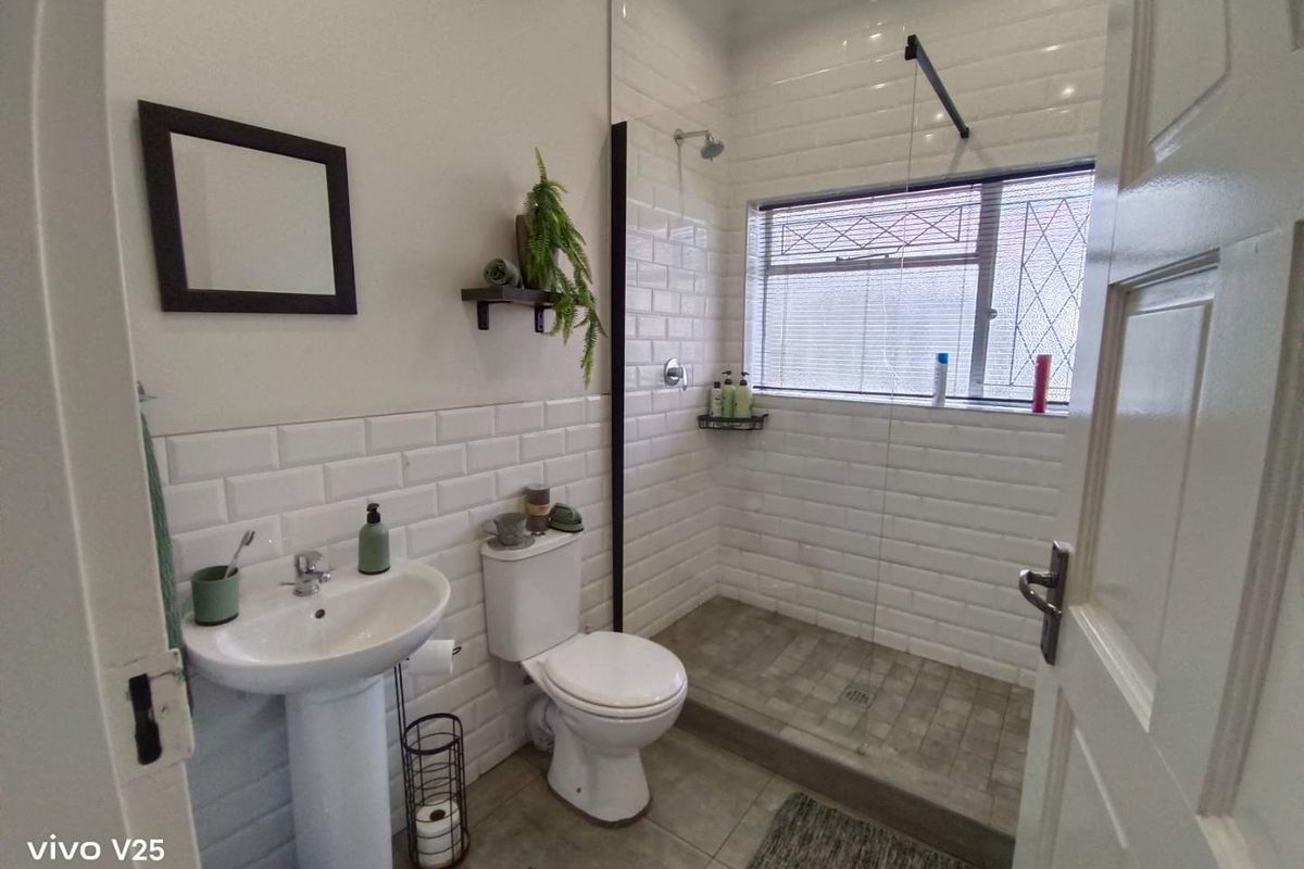 A modern bathroom featuring white subway wall tiles, a walk-in shower with a glass screen, a pedestal basin, and a toilet.