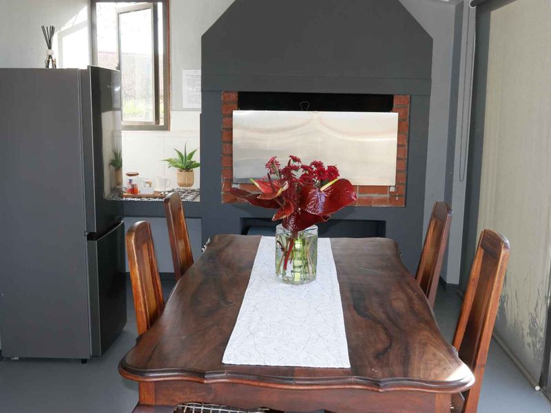 Covered patio area featuring a built-in brick braai with stainless steel finish, tiled flooring, and large sliding glass doors providing access to the garden.