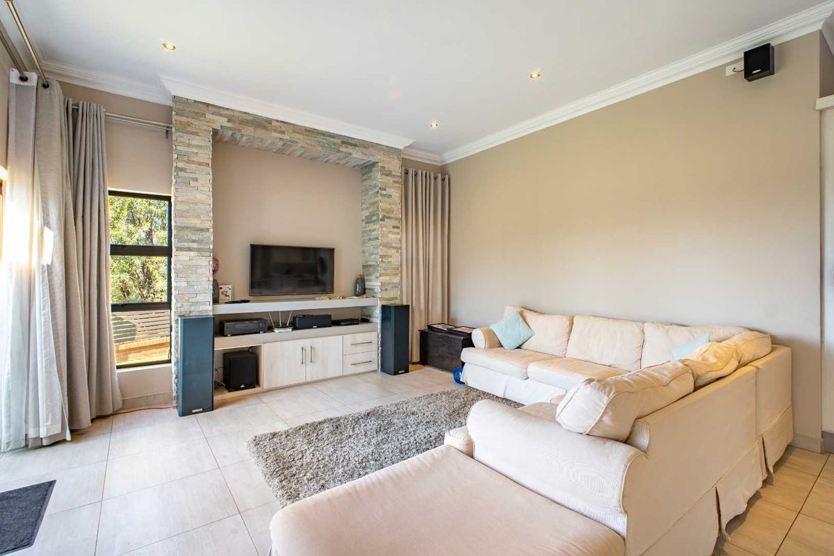 Spacious living room featuring a built-in stone-clad media unit, tiled flooring, recessed downlighting, and large windows with neutral curtains.