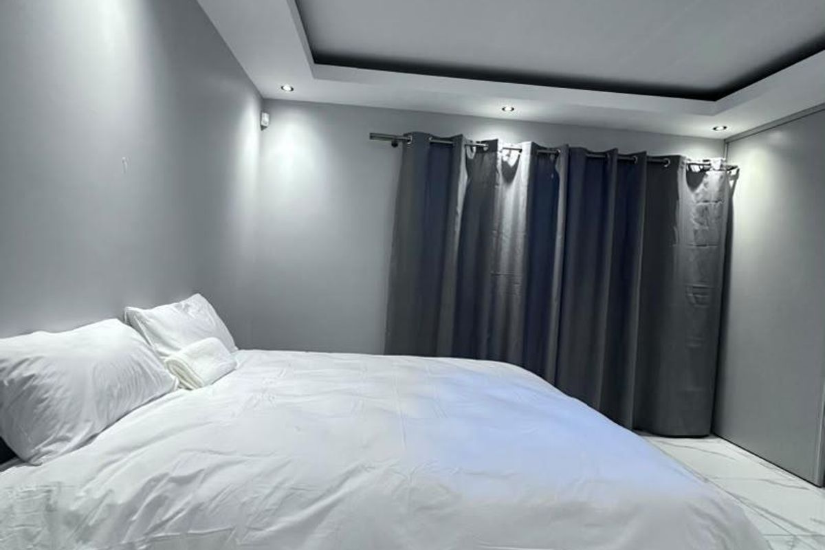 A modern bedroom featuring recessed tray ceiling lighting, marble-look floor tiles, and built-in wardrobe storage.