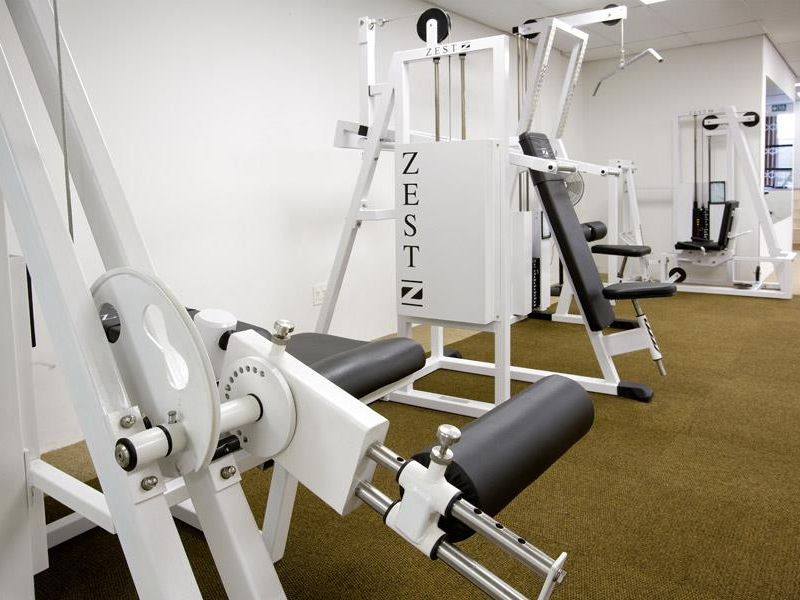 A dedicated gym space featuring carpeted flooring and a suspended ceiling, equipped with multiple professional-grade strength training machines.