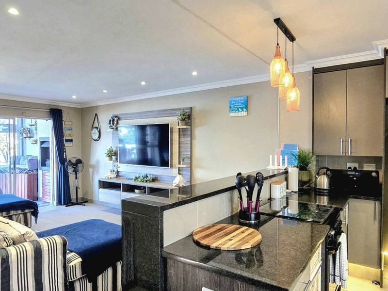 Open-plan living area featuring a modern kitchen with granite countertops and built-in cabinetry, flowing seamlessly into a comfortable lounge with access to the patio.