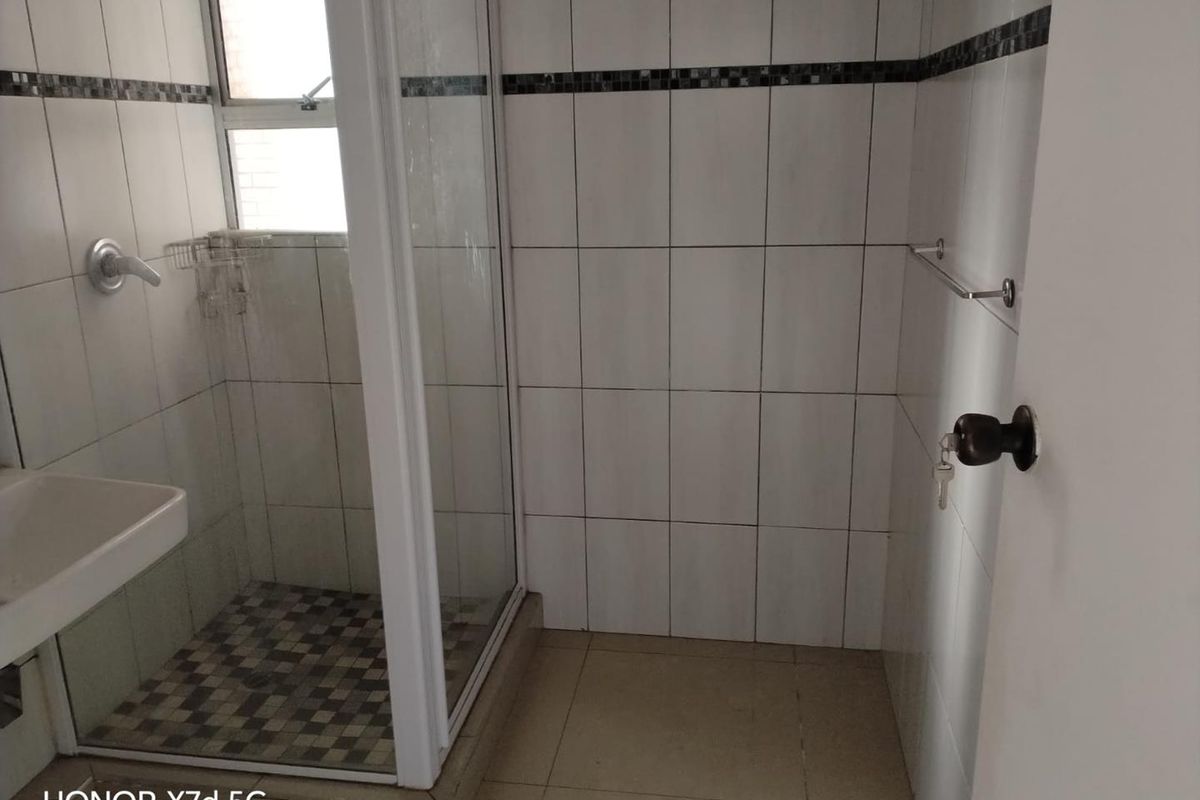 A functional bathroom featuring a shower enclosure, wall-mounted basin, and neutral tiled finishes throughout.