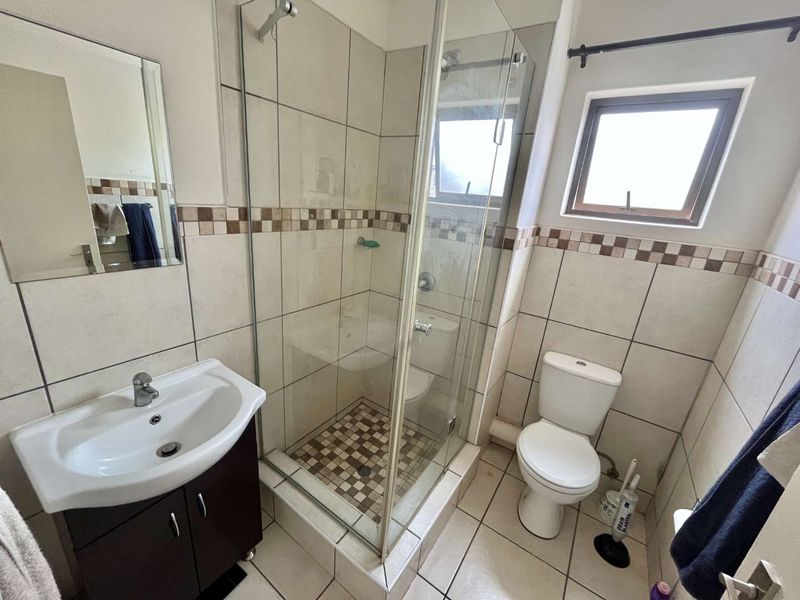 A functional bathroom featuring a glass-enclosed shower, vanity cabinet with basin, toilet, and neutral ceramic tiling throughout.