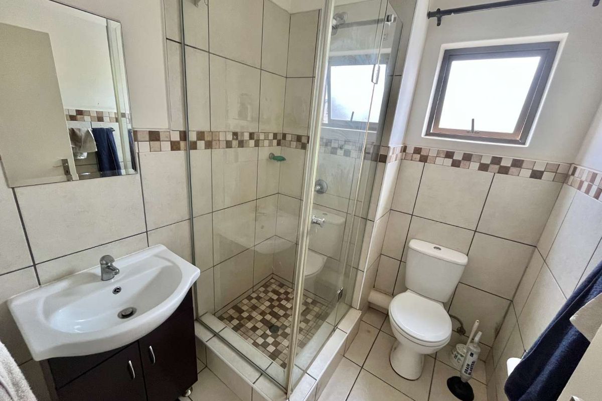 A functional bathroom featuring a glass-enclosed shower, vanity cabinet with basin, toilet, and neutral ceramic tiling throughout.