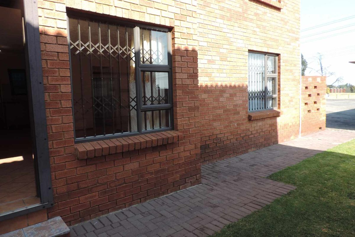 Exterior view of the townhouse featuring face-brick facade, security gates on windows, and a paved walkway leading to the entrance.