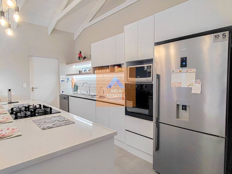 Modern kitchen featuring a central island with gas hob, sleek white cabinetry, subway tile backsplash, and high-end built-in appliances under vaulted ceilings.