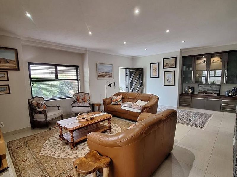Spacious living room featuring neutral tiled flooring, recessed downlighting, and custom built-in display cabinetry, offering a bright and well-maintained living environment.