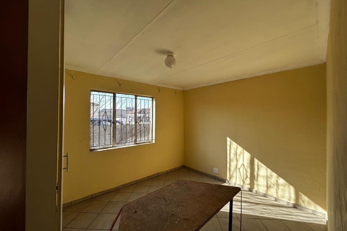 An empty bedroom featuring tiled flooring and security bars on the window, requiring cosmetic updates to the wall finishes.