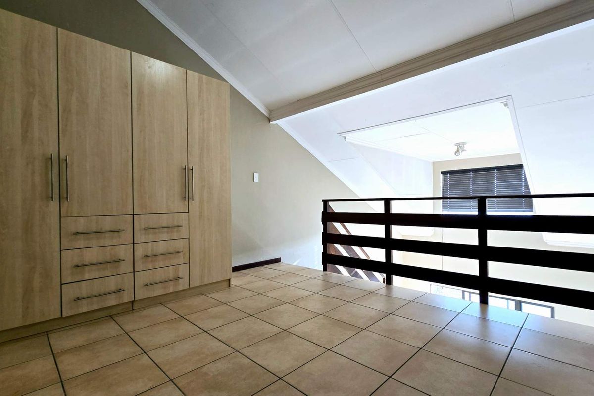 A mezzanine level featuring built-in light wood cabinetry, tiled flooring, and a dark timber balustrade overlooking the lower living area.