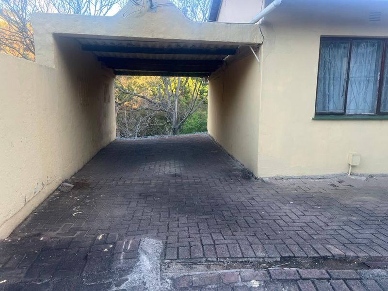 A covered carport area with paved flooring and visible exterior wall cracking, providing sheltered parking space for the townhouse.