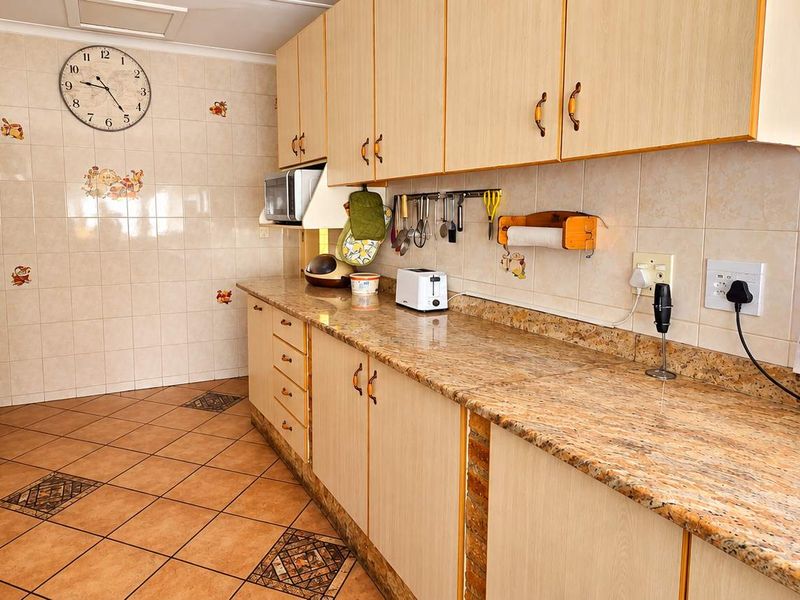 A functional kitchen featuring granite countertops, laminate cabinetry, tiled backsplash, and ceramic tile flooring with a built-in hob and extractor fan.