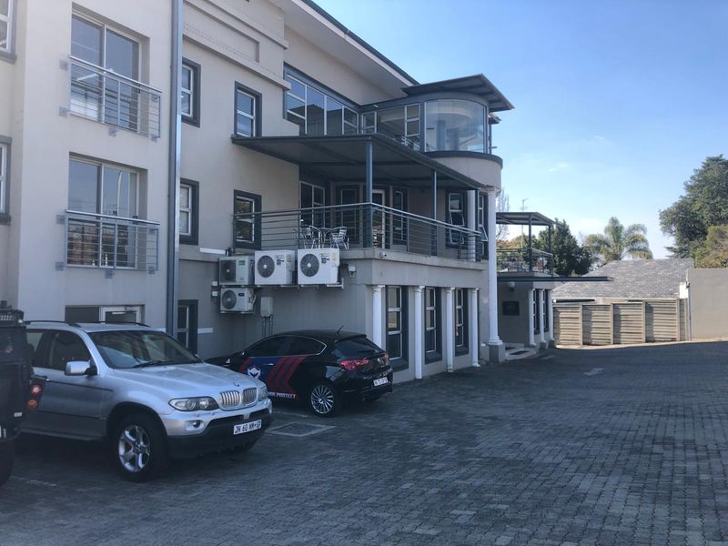 Rear view of the office building featuring paved parking, multiple balconies with metal railings, and external air conditioning units.