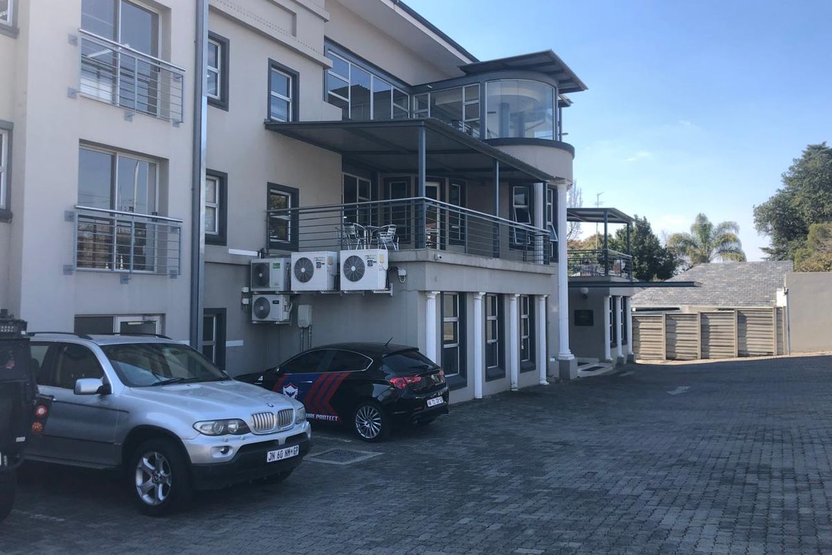 Rear view of the office building featuring paved parking, multiple balconies with metal railings, and external air conditioning units.