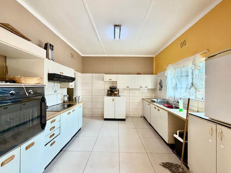 Functional kitchen featuring built-in oven, extractor fan, hob, and double sink with ample cabinetry and tiled finishes throughout.