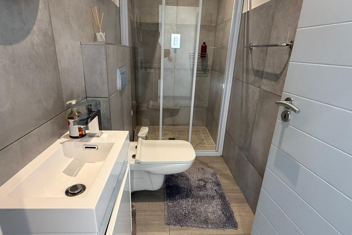 Modern bathroom featuring a wall-mounted vanity, a sleek wall-hung toilet, and a glass-enclosed shower with contemporary grey tiling.