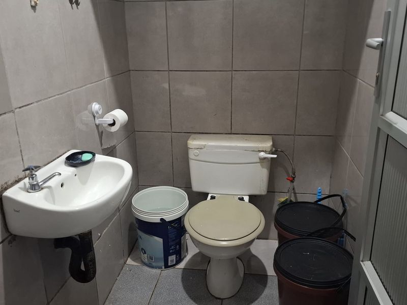 A compact bathroom featuring tiled walls and floors, a wall-mounted basin, and a standard toilet, requiring some cosmetic updates to improve its overall condition.