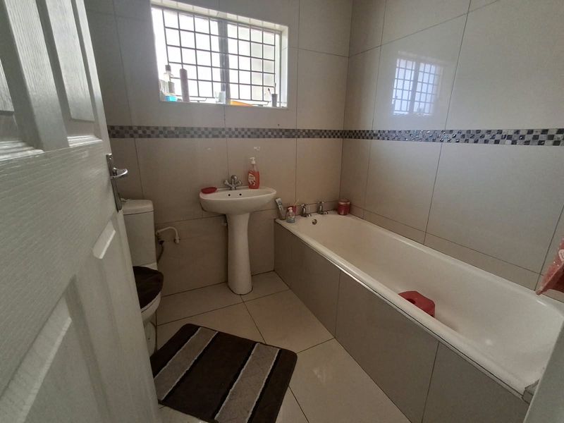 A functional bathroom featuring a pedestal basin, bathtub, and toilet with neutral wall and floor tiling.