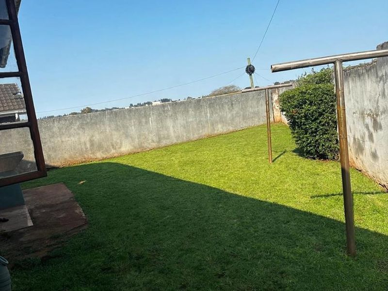 A rear garden area featuring a lawn and perimeter boundary walls with metal washing line infrastructure.