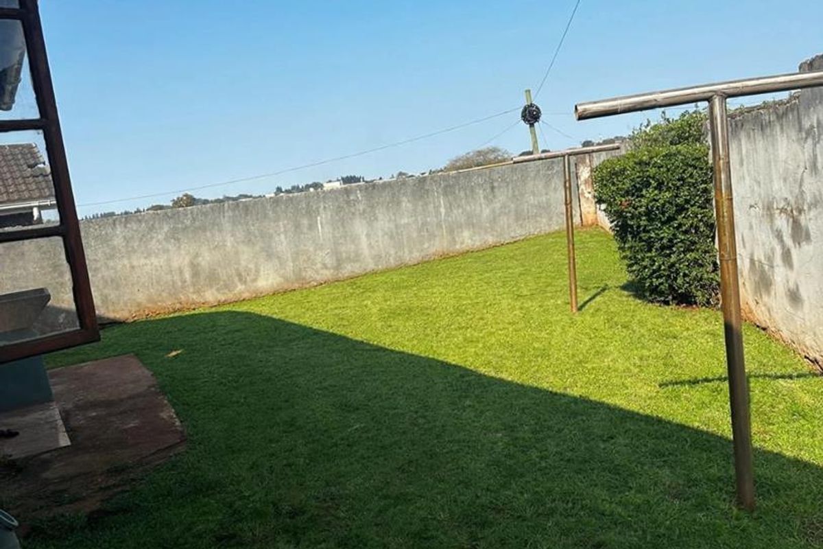 A rear garden area featuring a lawn and perimeter boundary walls with metal washing line infrastructure.