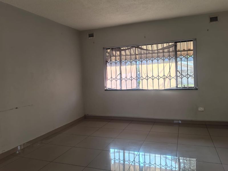 An empty living room featuring tiled flooring and a window fitted with a security gate, offering a blank canvas for interior design.