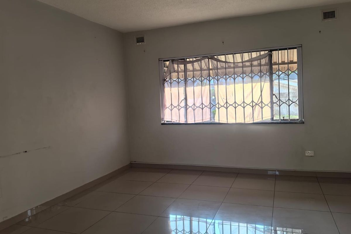 An empty living room featuring tiled flooring and a window fitted with a security gate, offering a blank canvas for interior design.