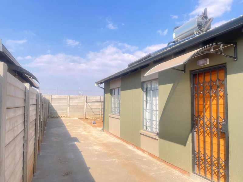 Rear exterior view of the property featuring a concrete walkway, security gate, and roof-mounted solar geyser system.