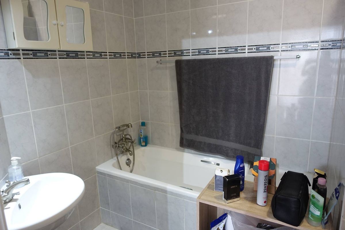 A functional bathroom featuring a bathtub with a mixer tap, a wall-mounted basin, and neutral wall tiling throughout.