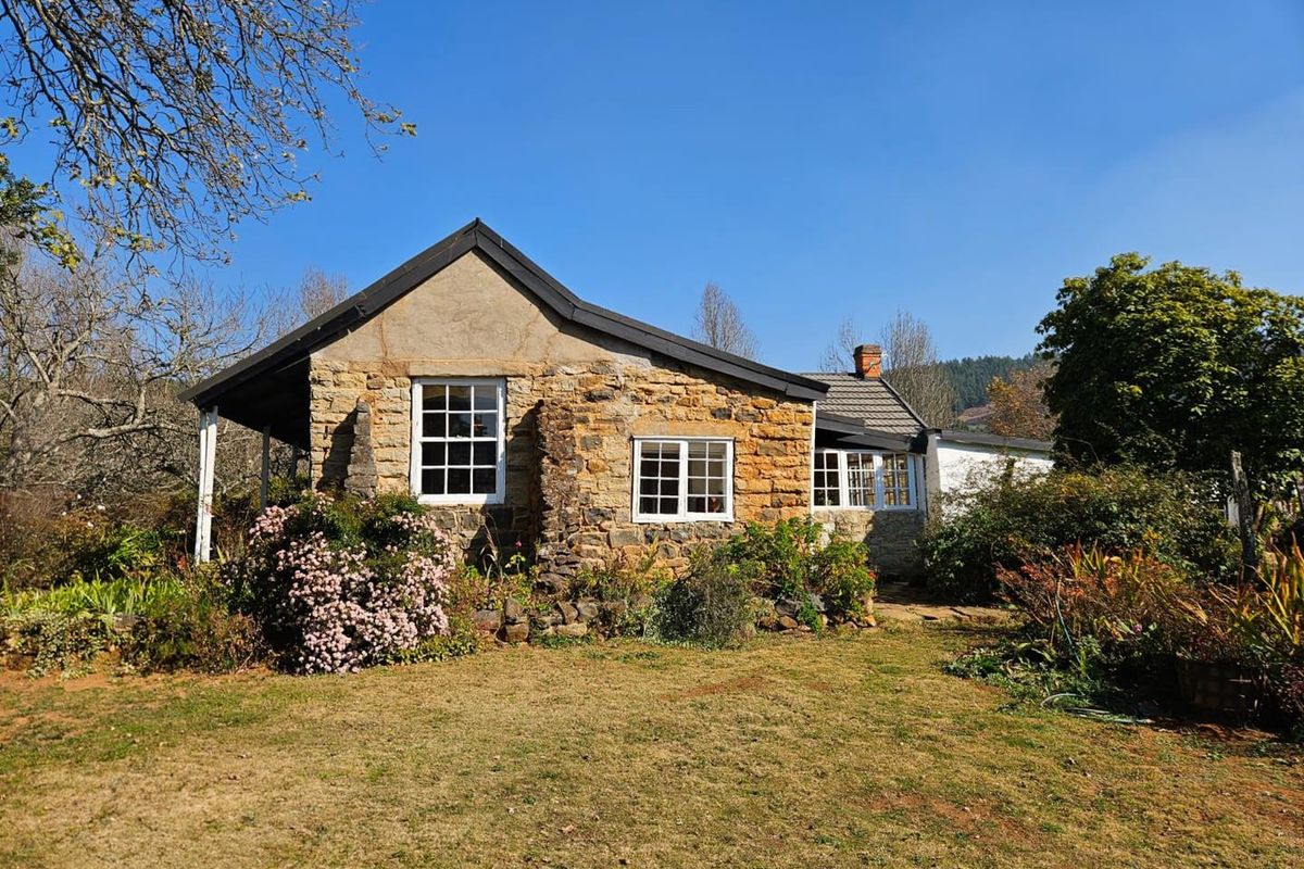 A charming stone-clad farmhouse exterior featuring classic sash windows, a covered patio area, and established garden surroundings.