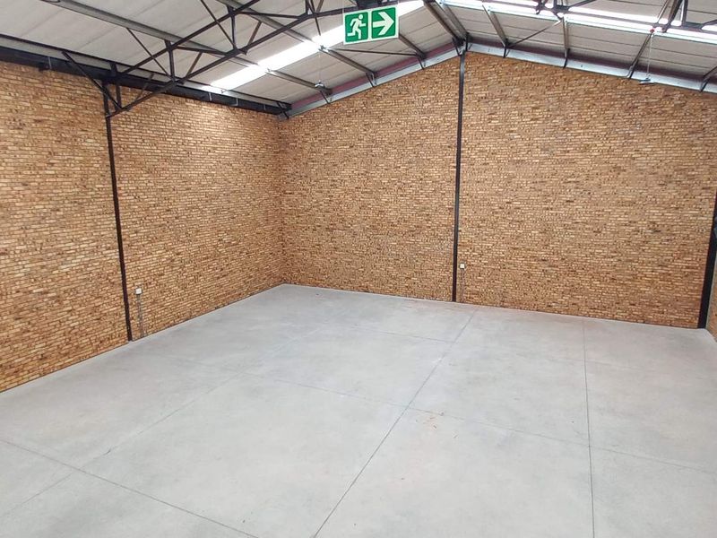 A spacious, empty industrial utility area featuring exposed brick walls, polished concrete flooring, and high-clearance steel roof trusses with natural lighting.