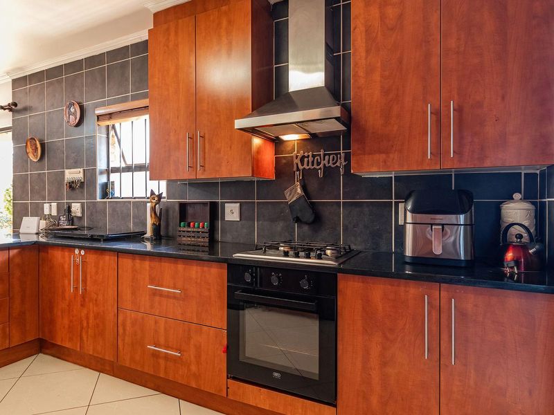 A functional kitchen featuring wooden cabinetry, granite countertops, a gas hob, built-in oven, and a stainless steel extractor fan with dark tiled splashbacks.