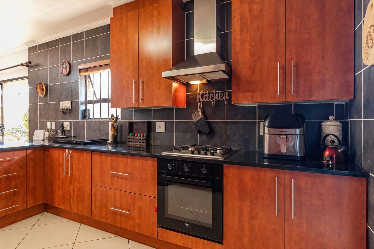 A functional kitchen featuring wooden cabinetry, granite countertops, a gas hob, built-in oven, and a stainless steel extractor fan with dark tiled splashbacks.